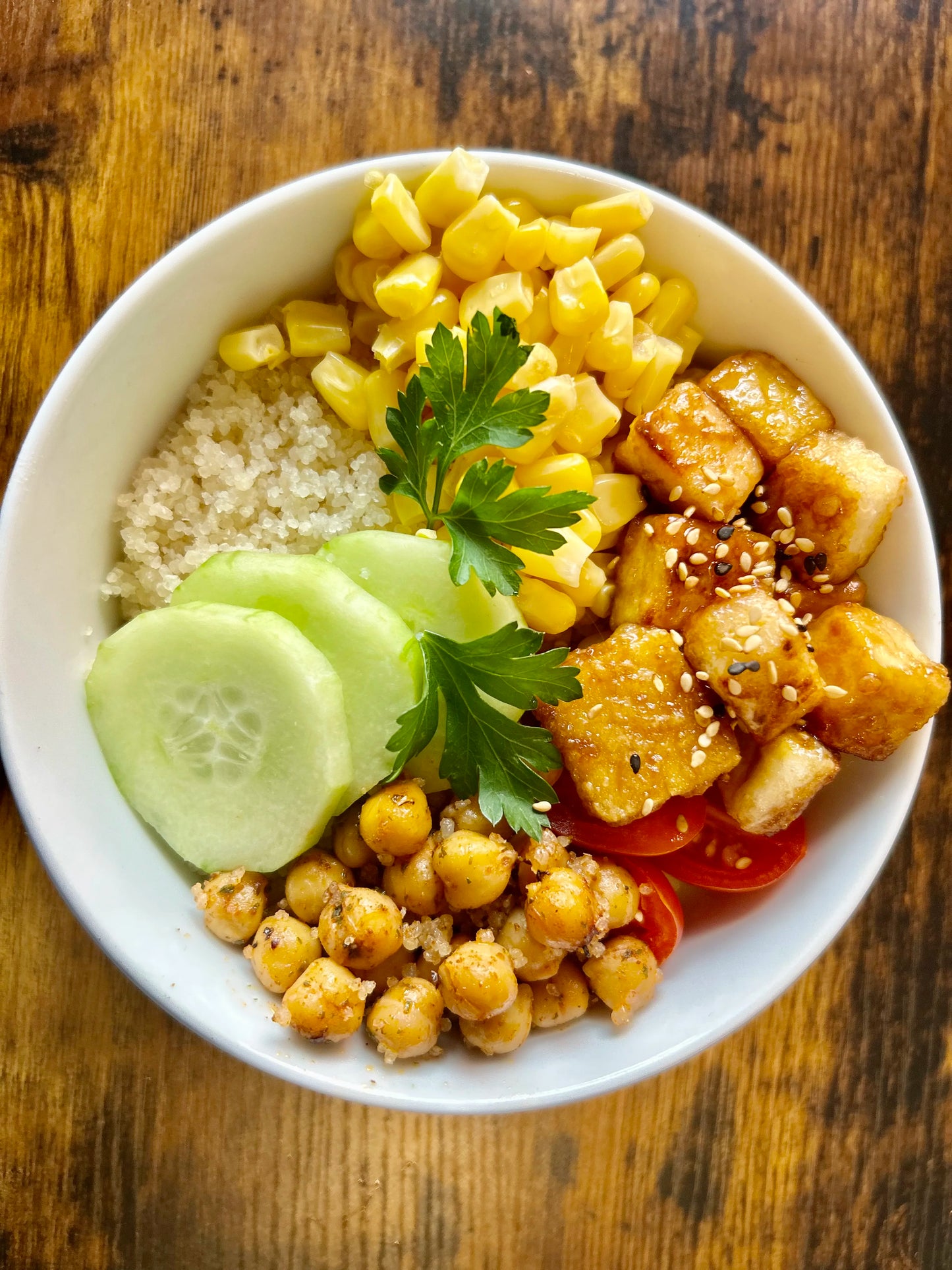 Bowl of Attiéké with corn, cucumber slices, chickpeas, tofu cubes, cherry tomatoes, and parsley garnish